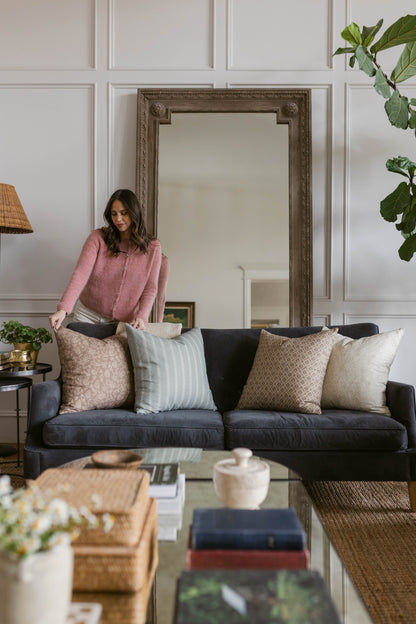Ornate silver-framed wall mirror with decorative molding and corner details mounted above a black sofa.