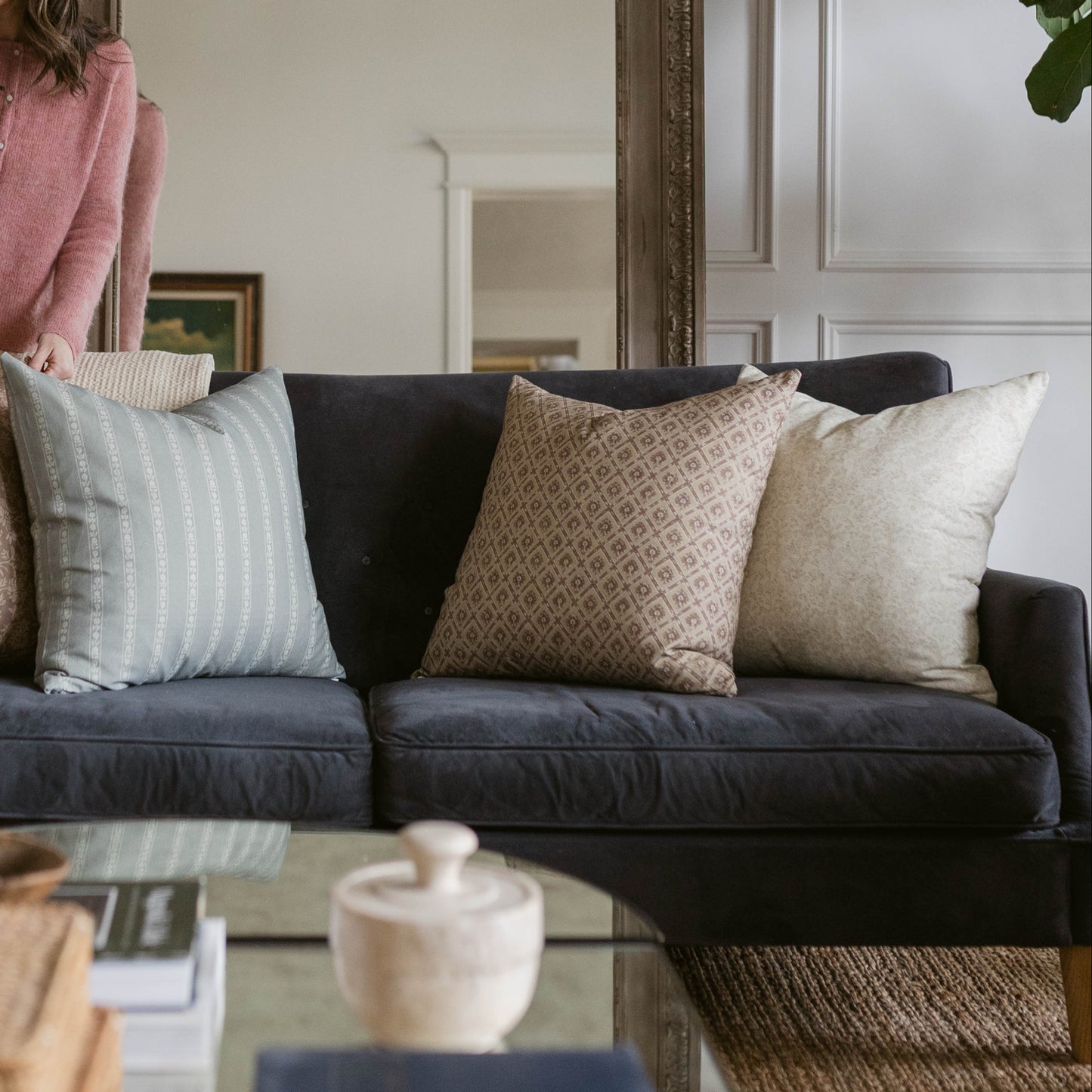 Three decorative pillows arranged on a dark gray sofa: striped light blue, geometric patterned tan, and solid cream.