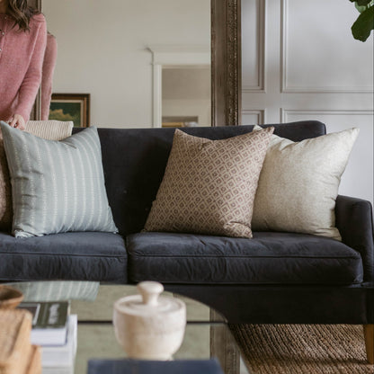 Three decorative pillows arranged on a dark gray sofa: striped light blue, geometric patterned tan, and solid cream.