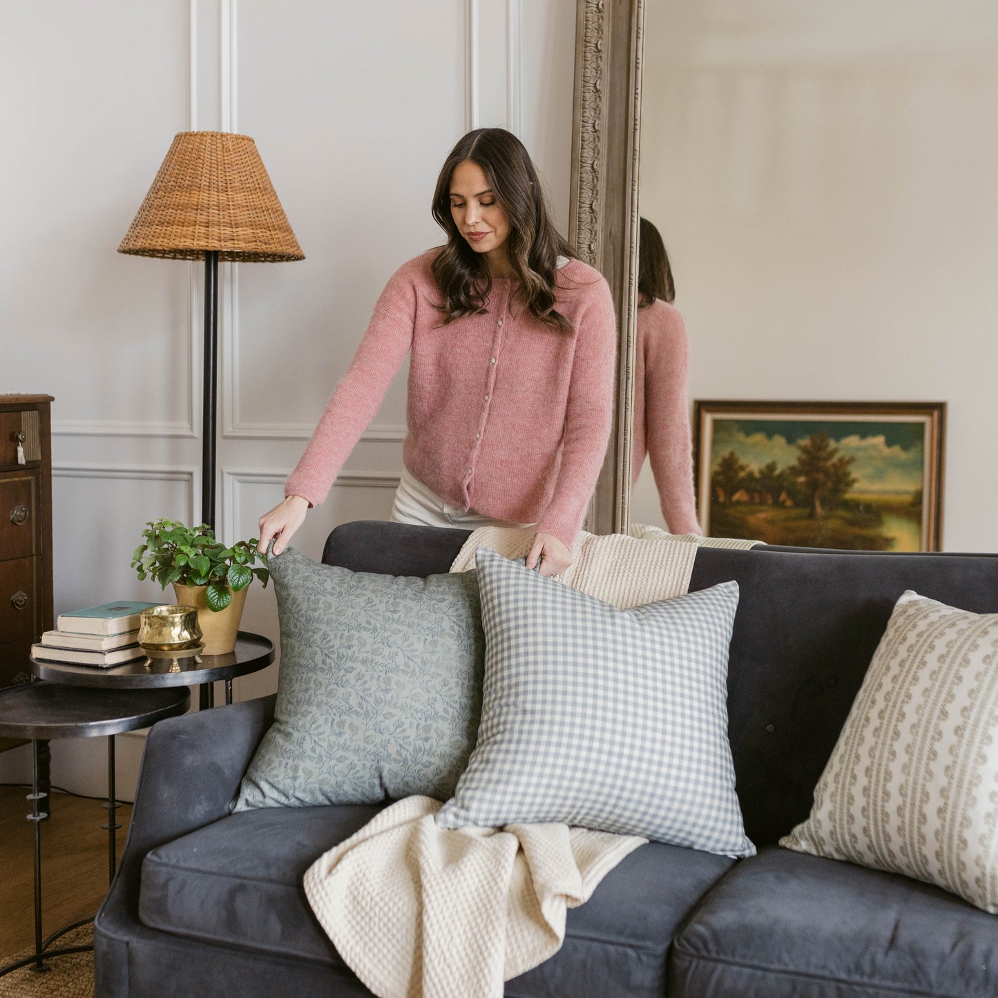 Four decorative pillows in gray gingham, gray floral, and cream textures arranged on a dark sofa.