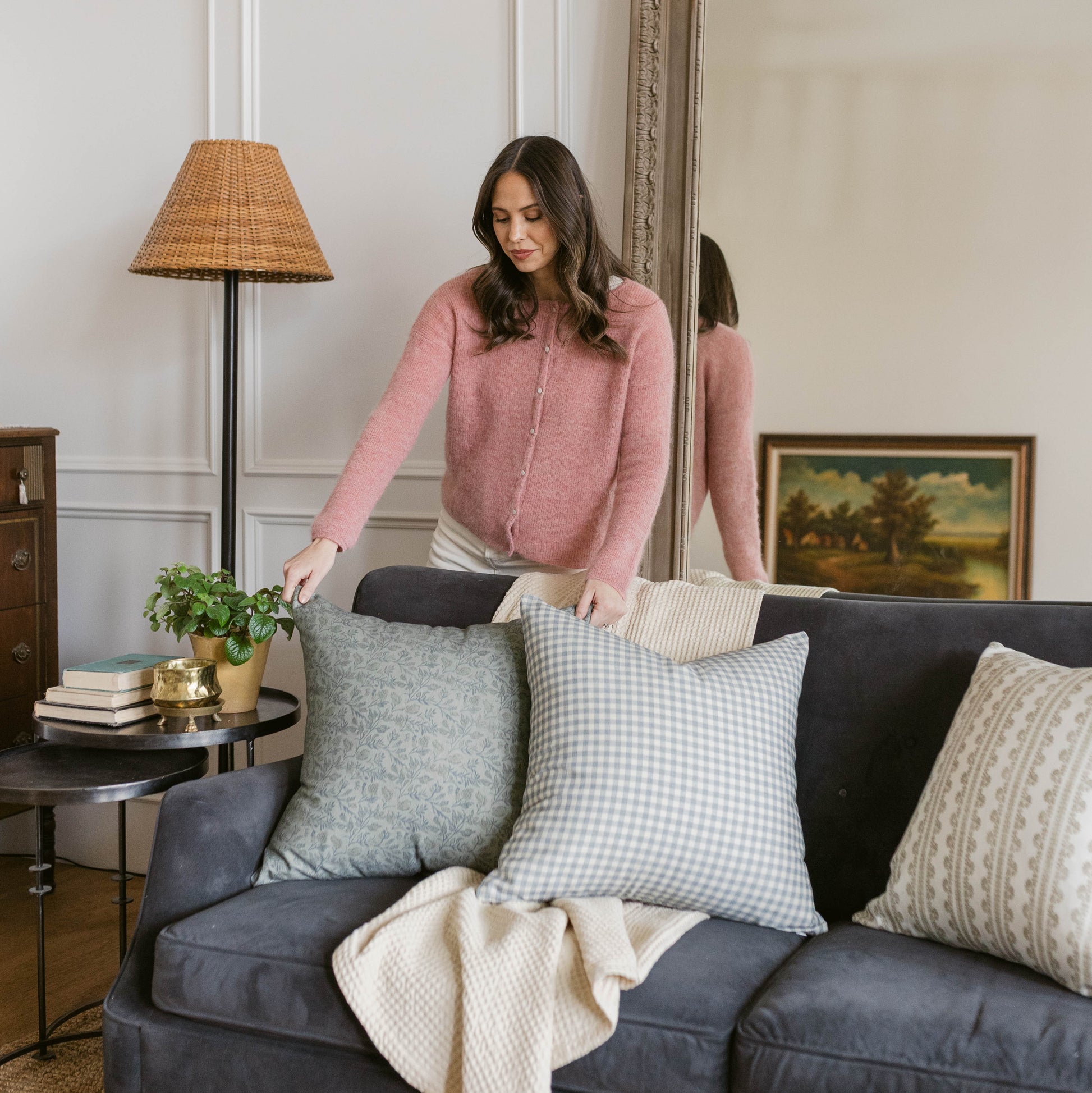 Dusty blue and white gingham check pillow on dark sofa with woman arranging decor.