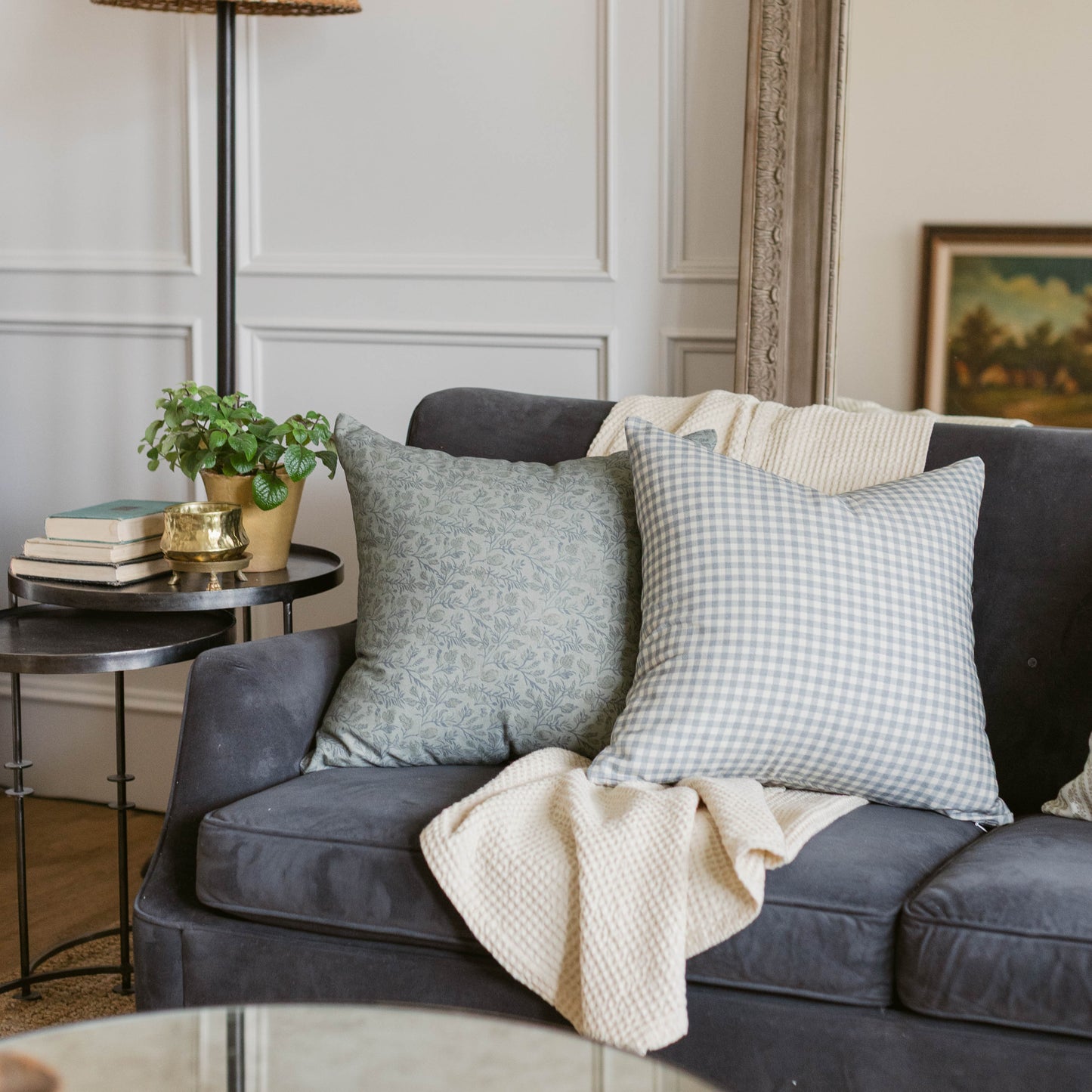 Dusty blue gingham patterned throw pillow displayed on a dark gray sofa.