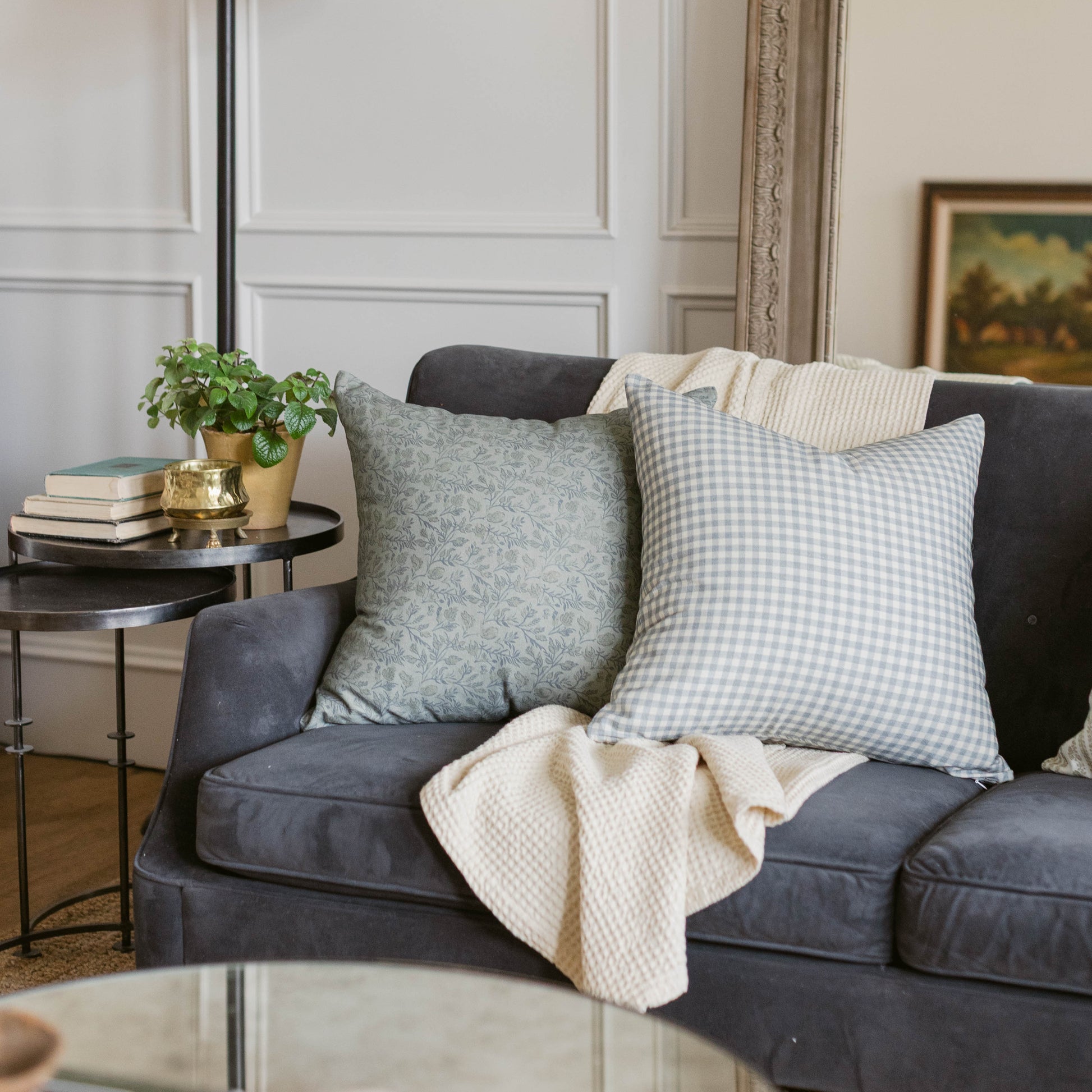 Four throw pillows in varying sizes displayed on a gray sofa, featuring floral and gingham patterns in sage and blue tones.