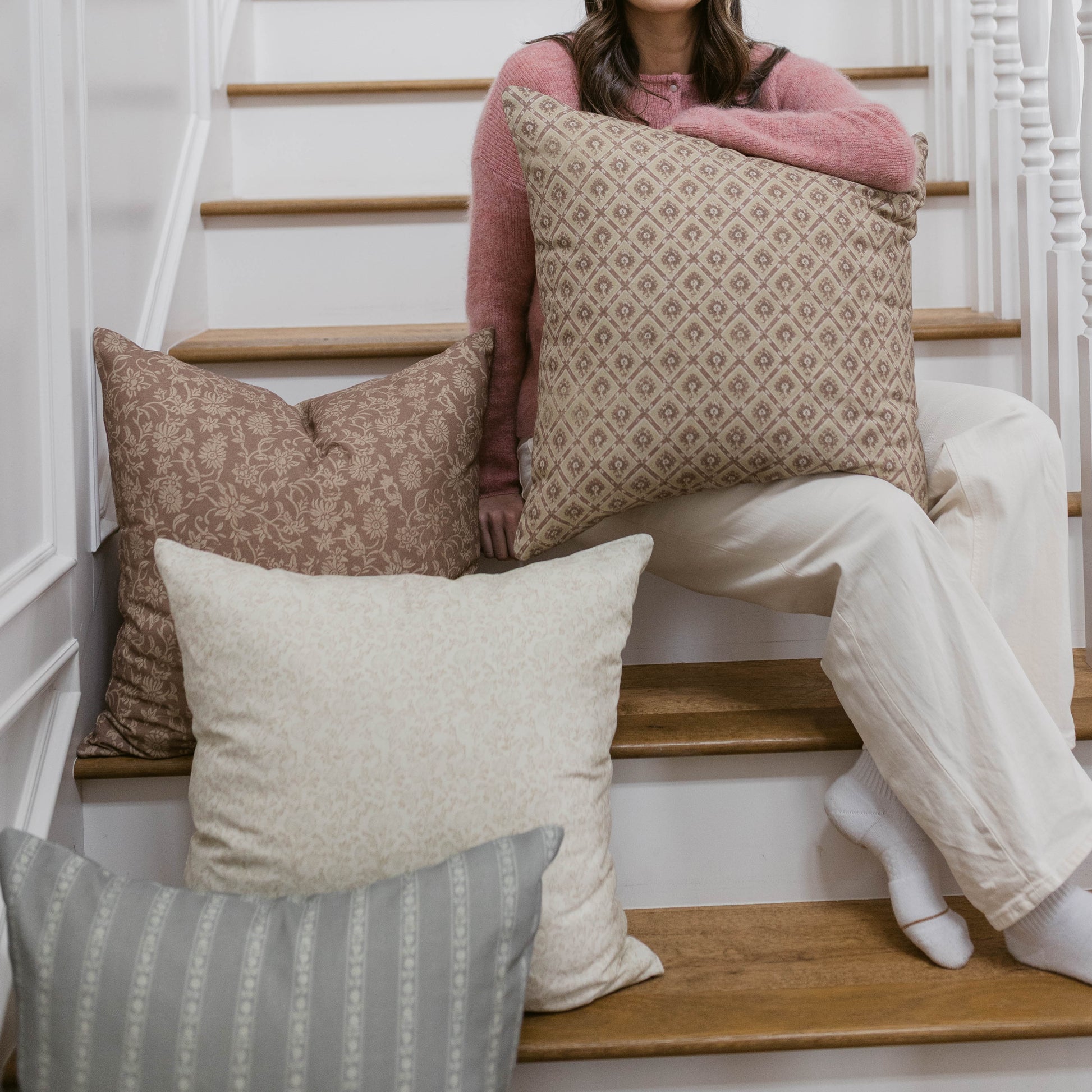Four decorative pillows in neutral tones with geometric and floral patterns, displayed on wooden stairs.