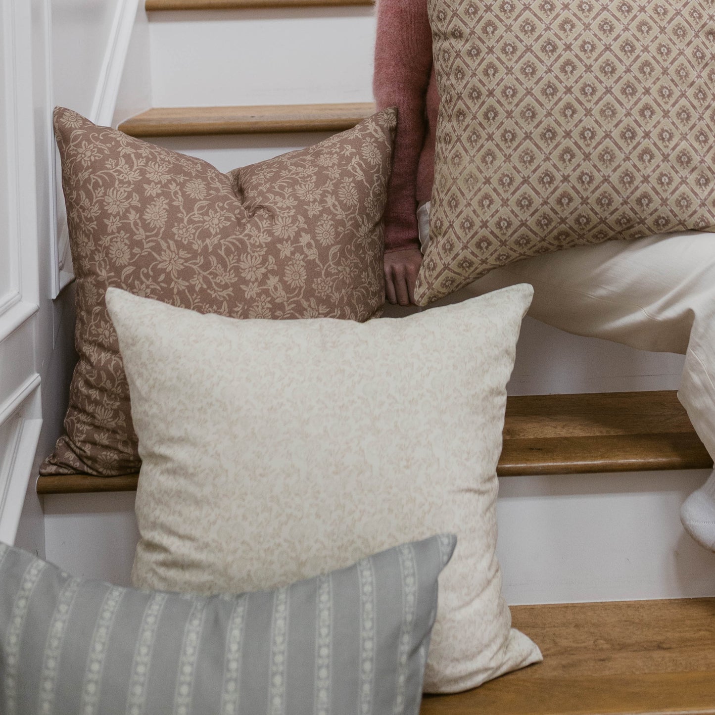 Cream-colored pillow with subtle texture displayed on a wooden bench next to patterned pillows in taupe and burgundy tones.
