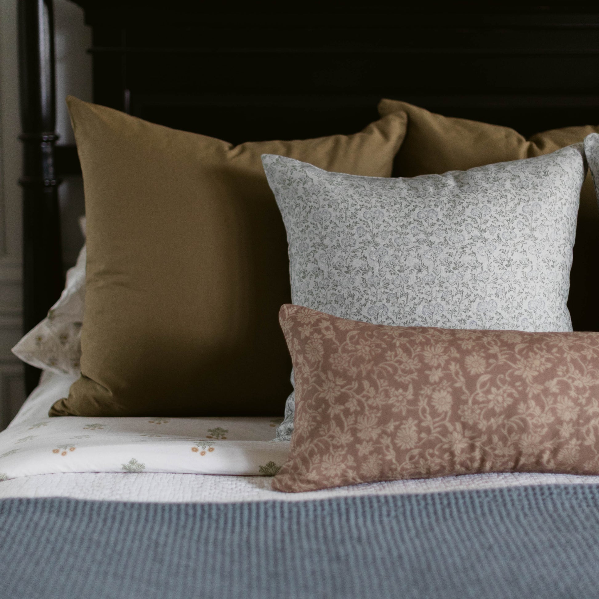 Tan linen pillow displayed on bed with gray textured and taupe patterned pillows.