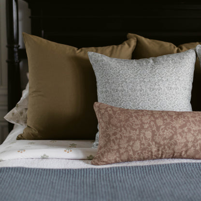 Tan linen pillow displayed on bed with gray textured and taupe patterned pillows.