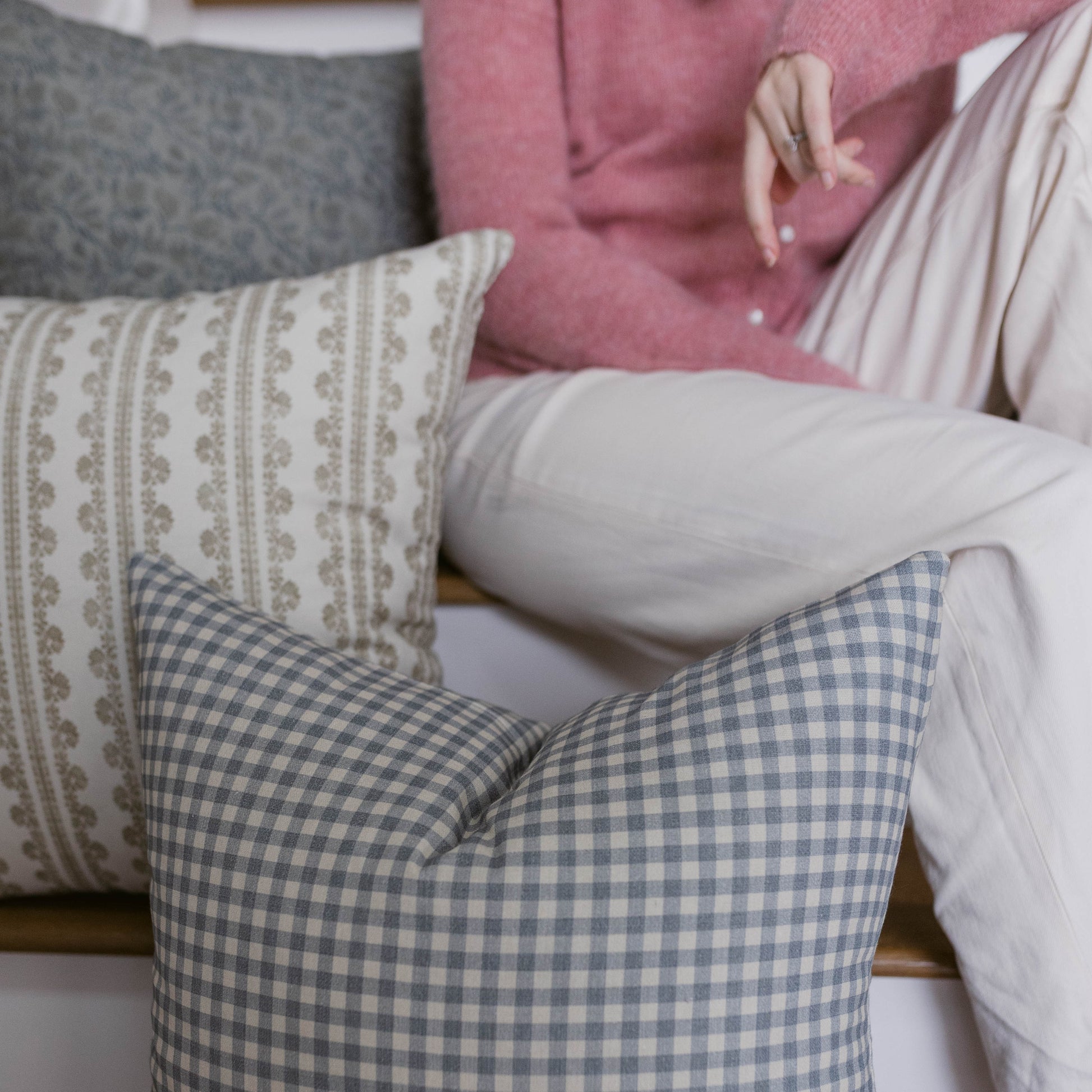 Four decorative pillows in cream, blue gingham, gray, and pink displayed on a couch.