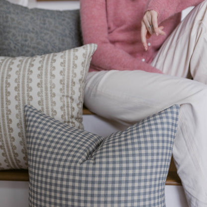 Four decorative pillows in cream, blue gingham, gray, and pink displayed on a couch.