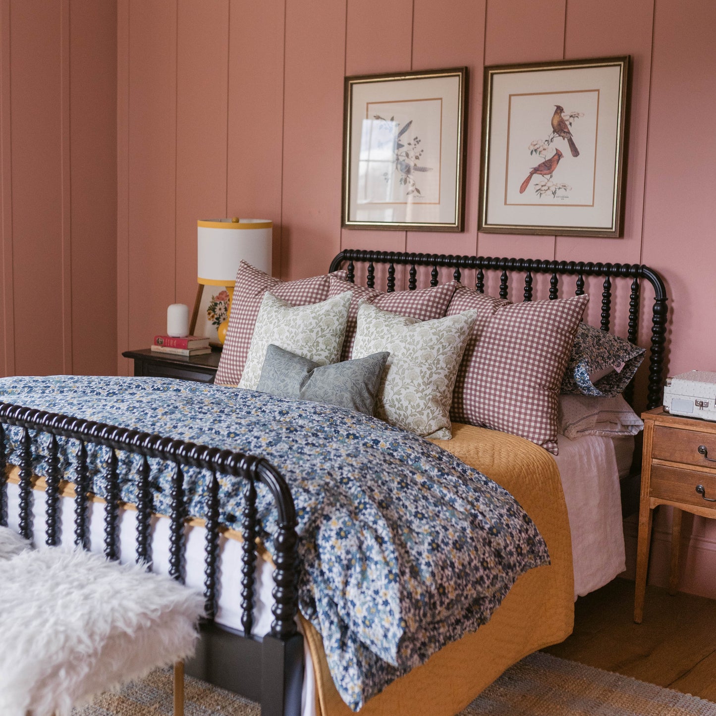 Two framed botanical bird prints with gold frames hung on pink paneled wall above bed.