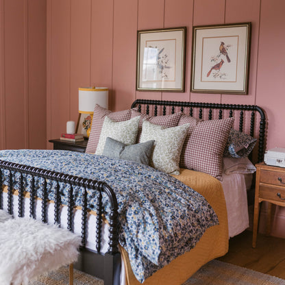 Two framed botanical bird prints with gold frames hung on pink paneled wall above bed.