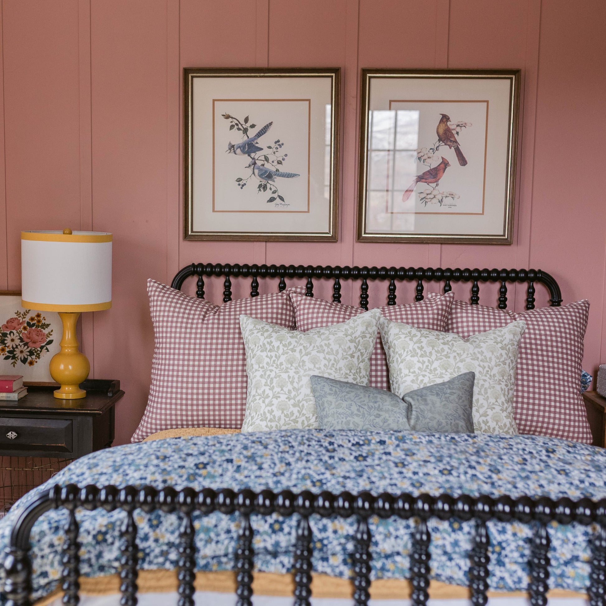 Rose and white gingham patterned pillow on a bed with black metal headboard in a bedroom setting.