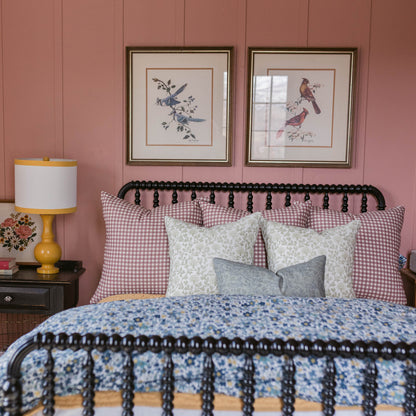 Rose and white gingham patterned pillow on a bed with black metal headboard in a bedroom setting.