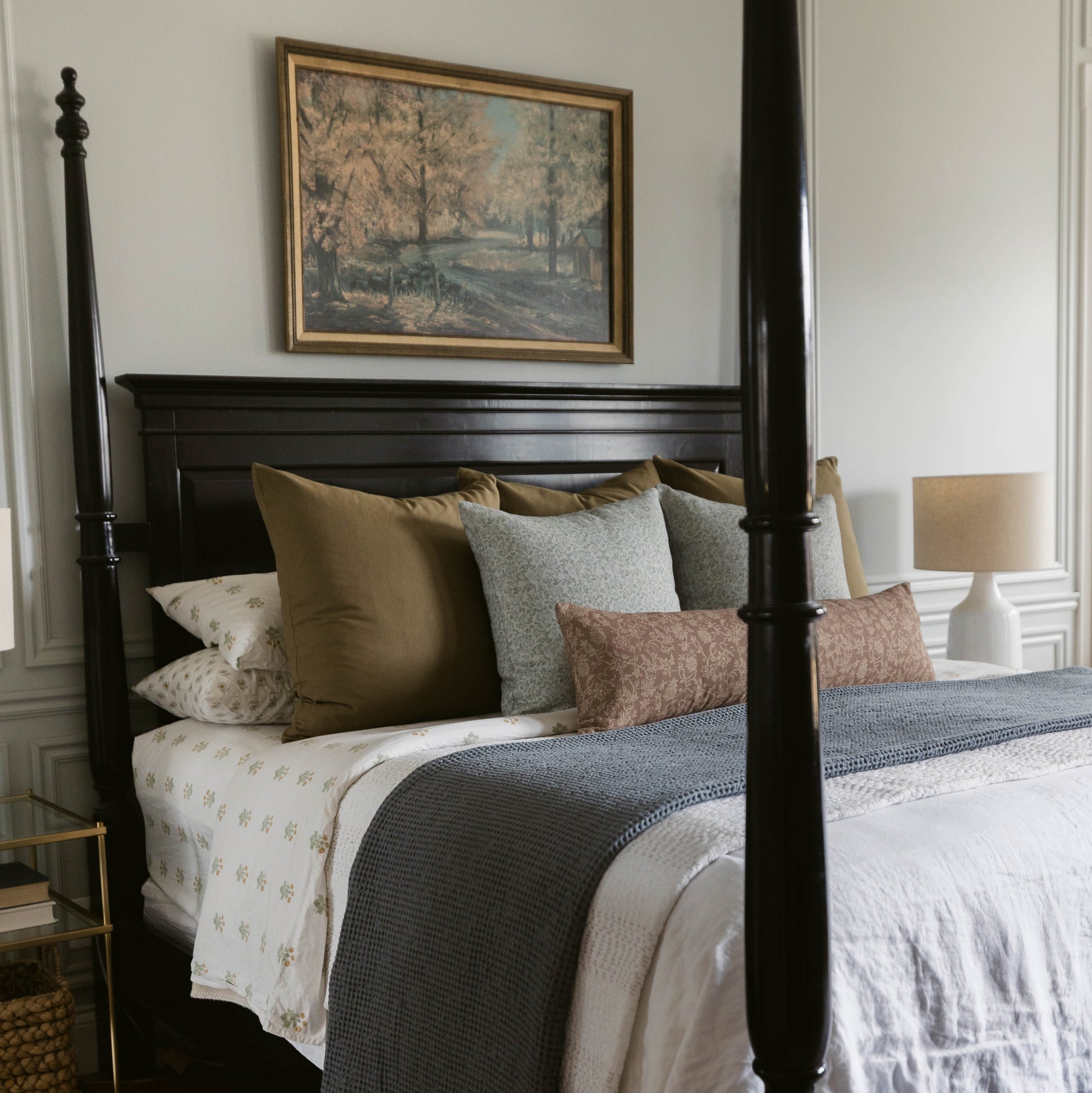 Styled bed with layered pillows and throw pillows in neutral tones including olive, gray, and brown linen.
