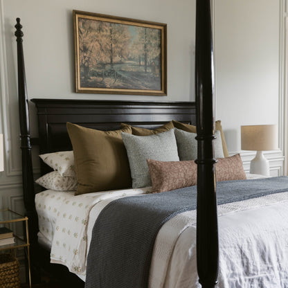 Styled bed with layered pillows and throw pillows in neutral tones including olive, gray, and brown linen.
