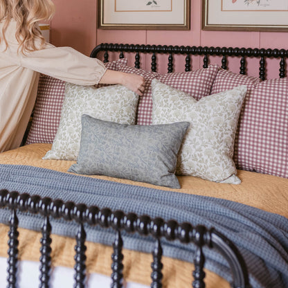 Rose gingham patterned pillow in mauve and white displayed on bed with coordinating pillows.