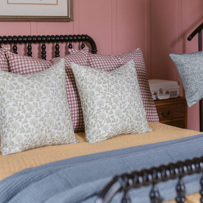 Decorative pillow with sage botanical print on linen, displayed on bed with gingham and patterned pillows.