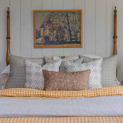 Dusty blue and white gingham pillows arranged on a bed with patterned accent pillows.