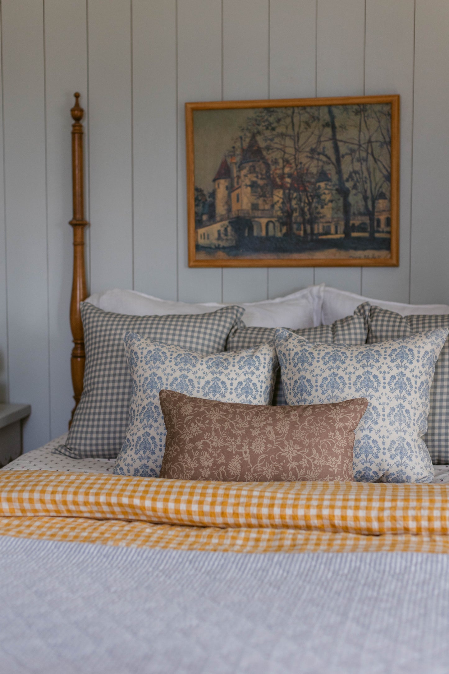 Linen pillow with blue damask pattern displayed on bed with gingham and striped bedding.