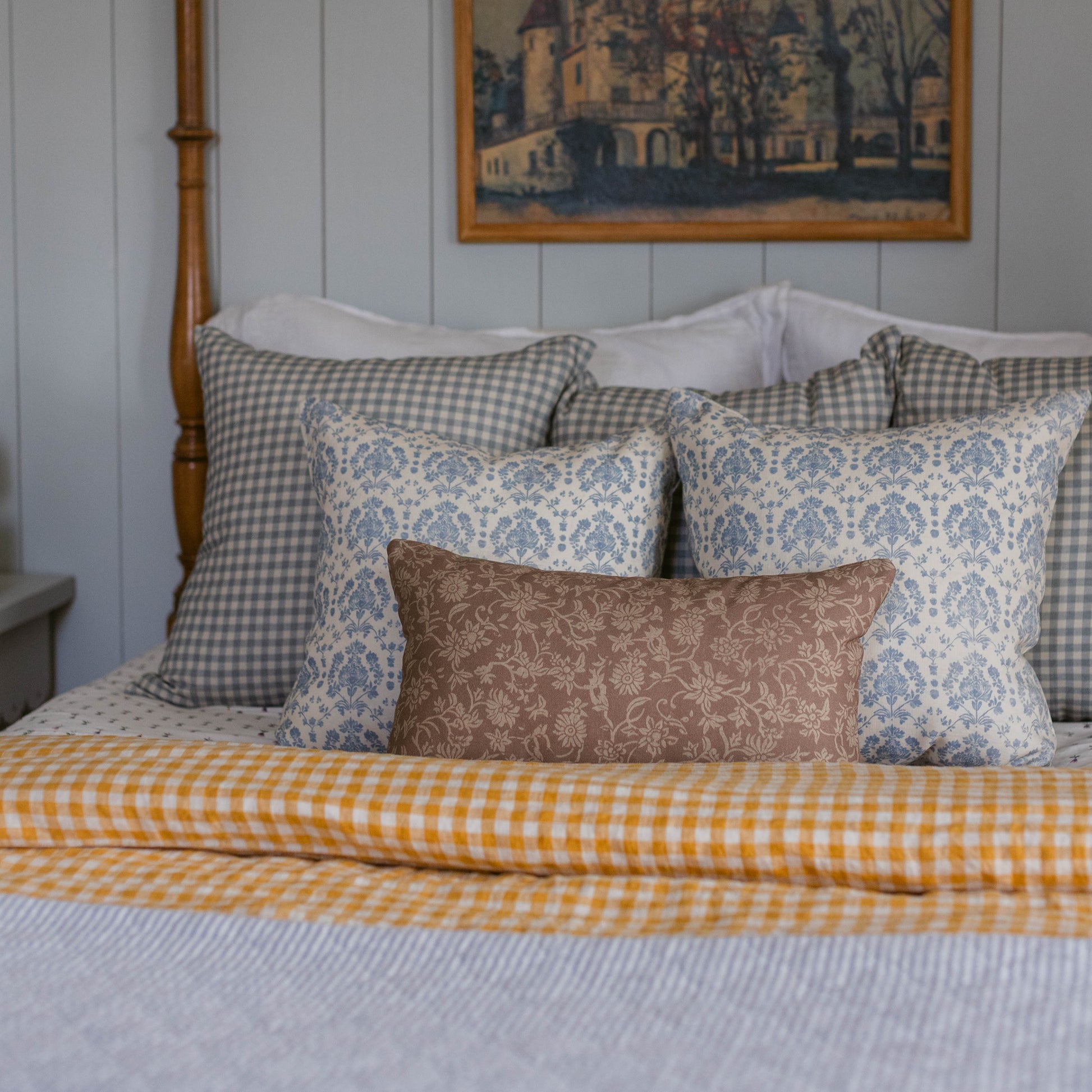 Dusty blue and white gingham check pillow displayed on a bed with coordinating patterned pillows.