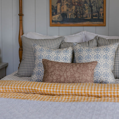 Dusty blue and white gingham check pillow displayed on a bed with coordinating patterned pillows.