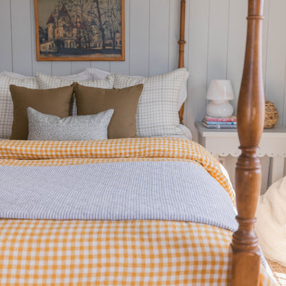 Bed with yellow gingham duvet, light blue striped sheet, olive and gray pillows, and wooden frame with nightstand.