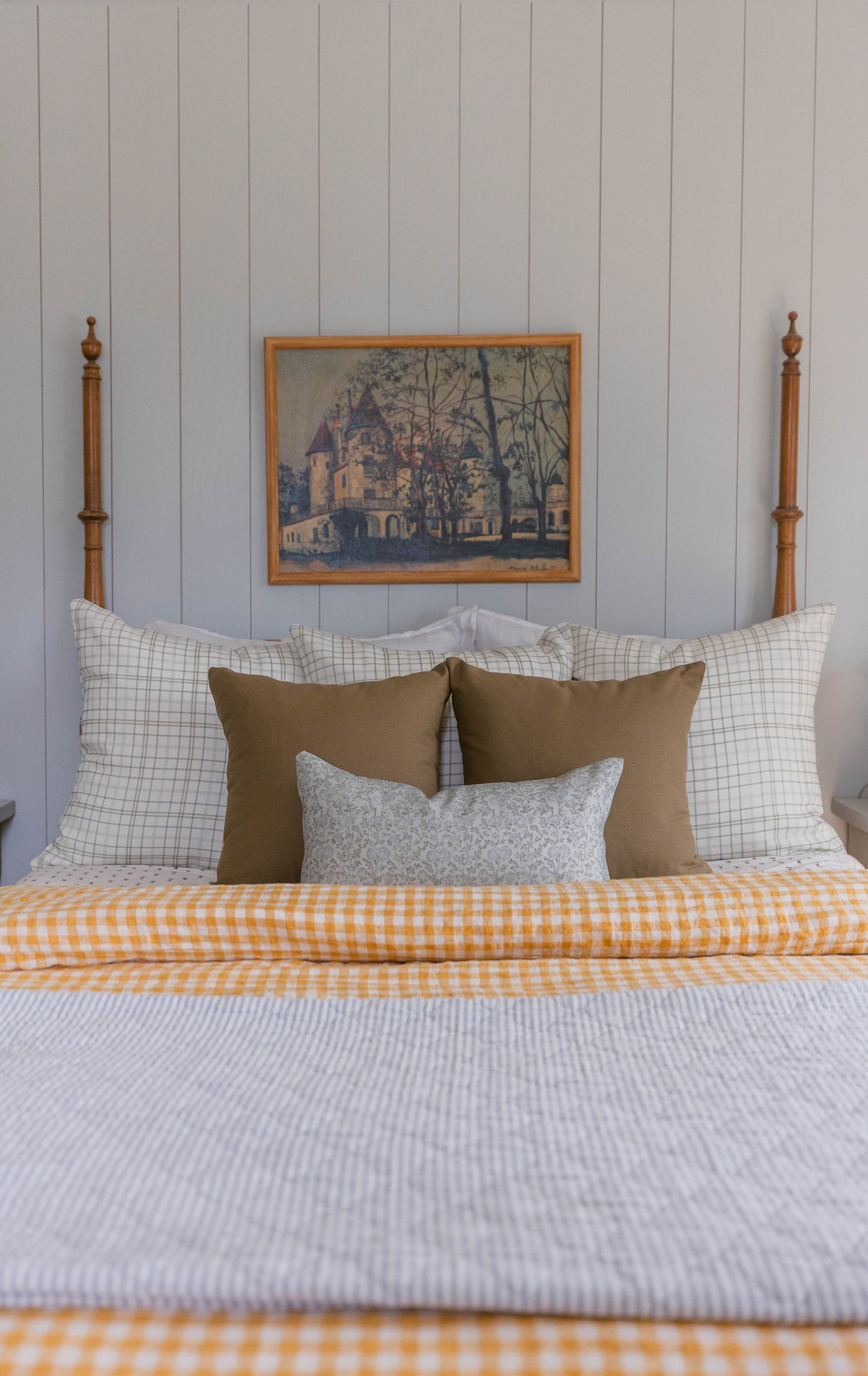 Tan linen pillows arranged on a bed with checkered and striped bedding.