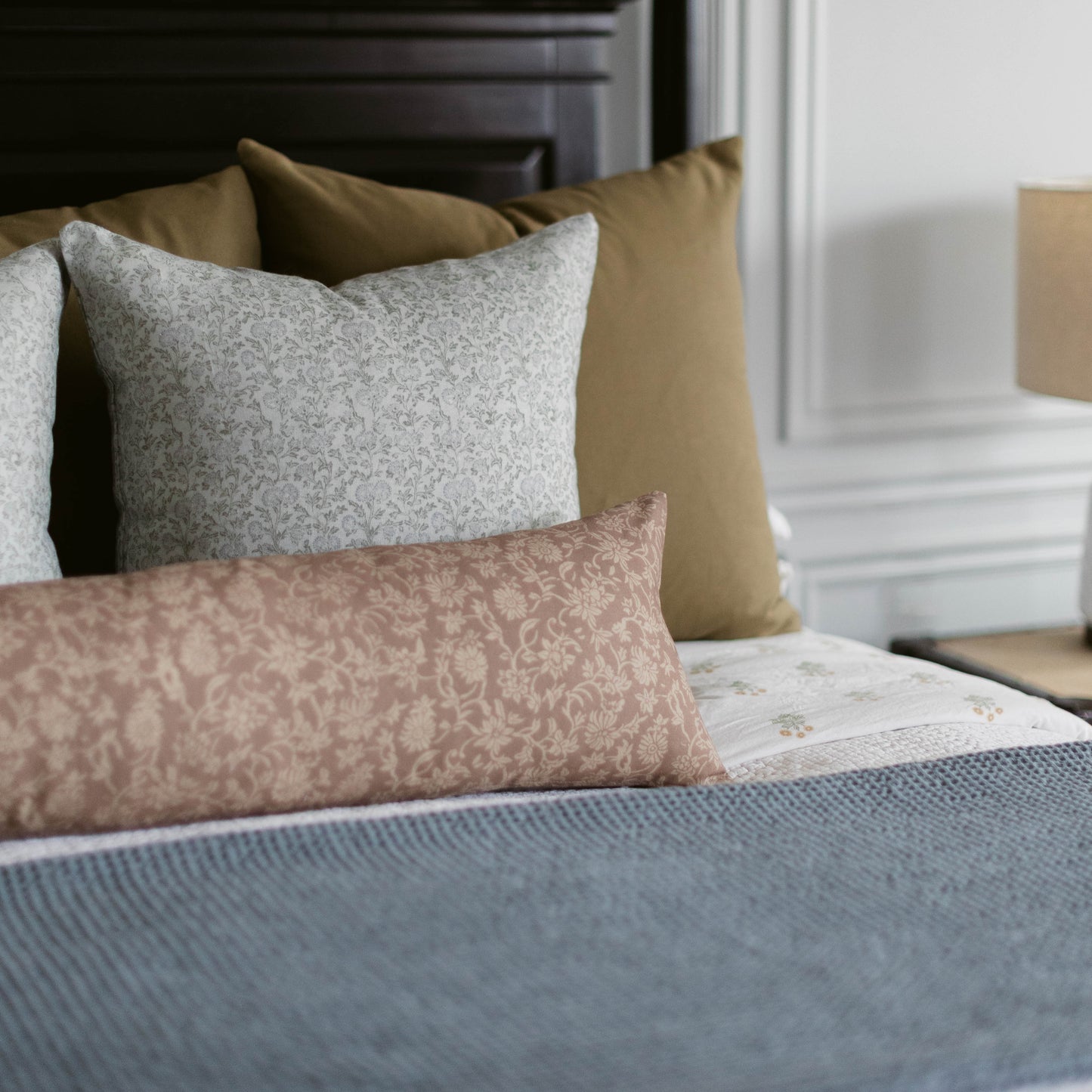 Rectangular throw pillow with damask pattern in mauve and cream, displayed on bed with coordinating pillows.