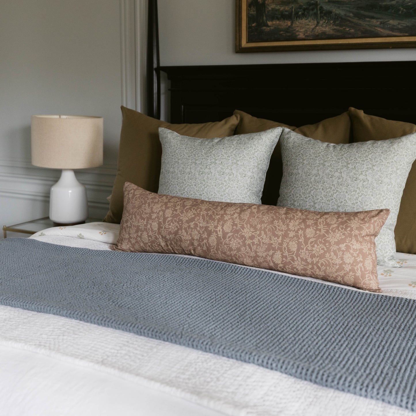 Bed styled with gray lumbar pillow, two light gray square pillows, olive pillows, and blue textured throw blanket.