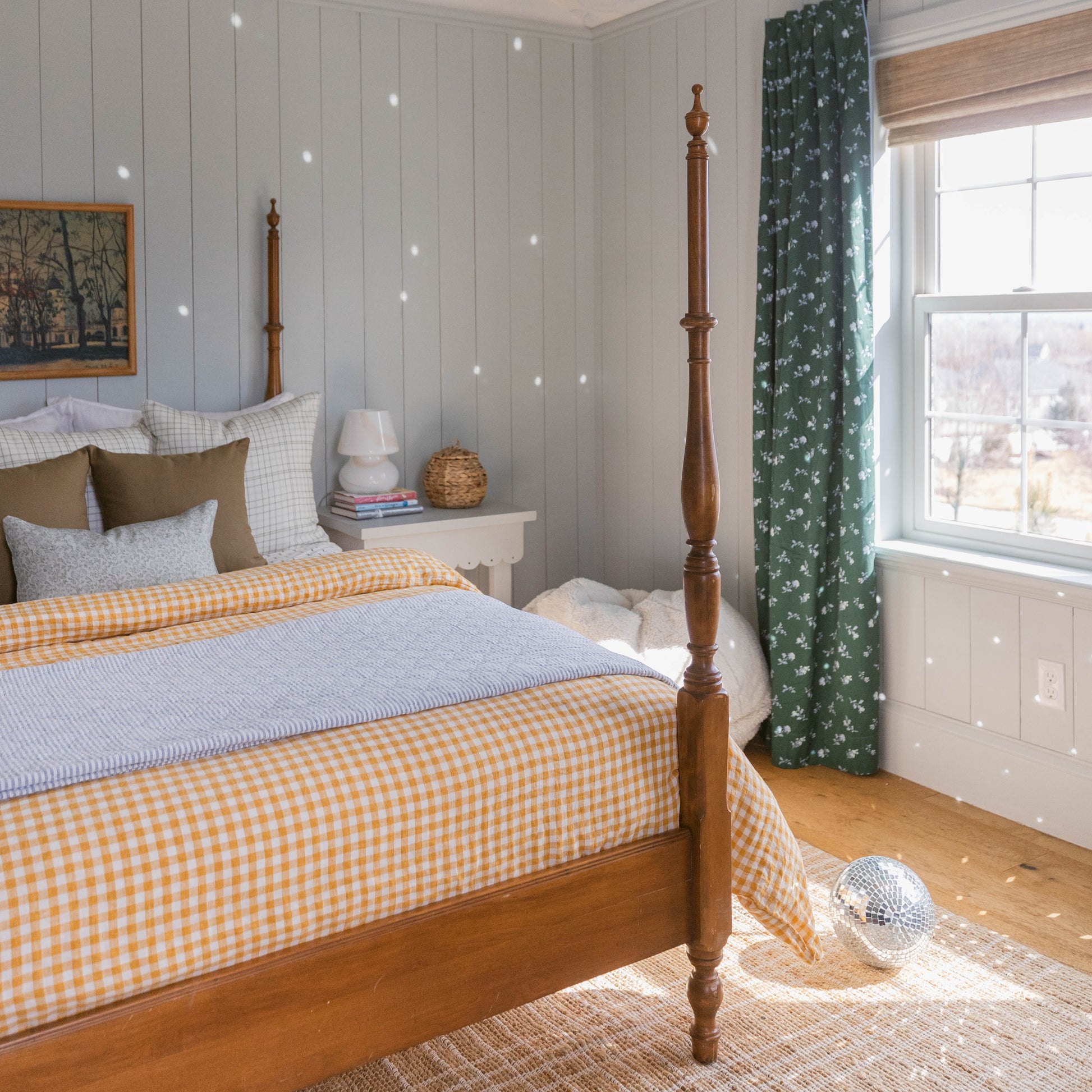 Bedroom with four-poster wooden bed, yellow and white checkered bedding, and pillows against light gray paneled wall.