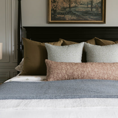 Bed with blue waffle-weave blanket, taupe and gray pillows, and damask patterned pillow sham against black headboard.