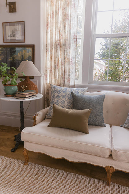 Beige linen pillow with subtle texture displayed on cream upholstered sofa with patterned pillows in living room setting.