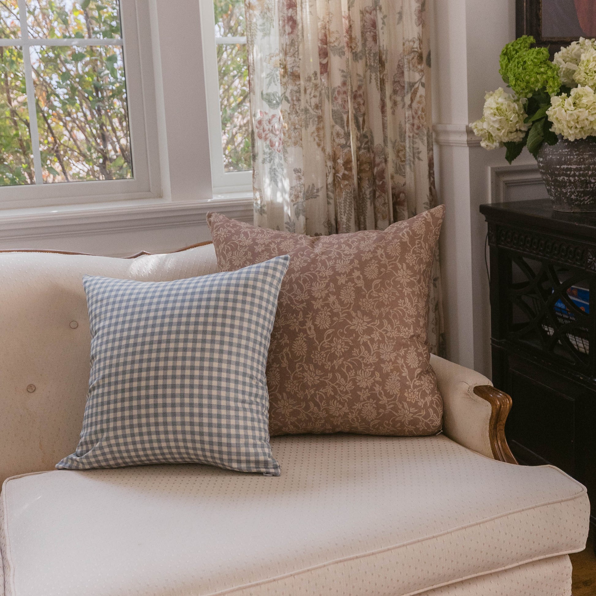 Dusty blue gingham check pillow displayed on a cream upholstered sofa next to a decorative brown patterned pillow.
