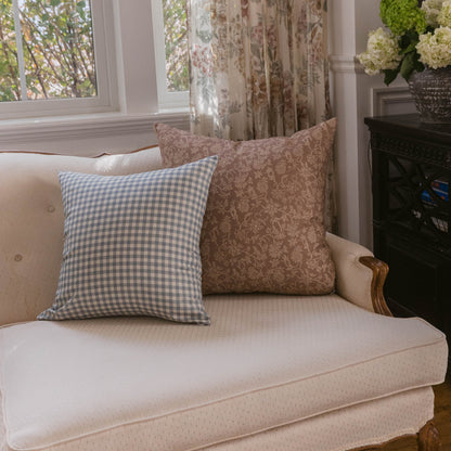 Two decorative pillows on a cream upholstered sofa: one with blue gingham pattern and one with taupe damask pattern.
