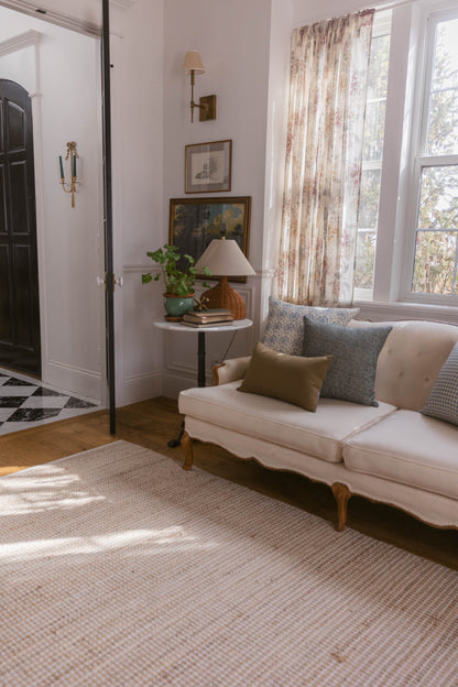 Beige linen pillow with olive and blue patterned pillows displayed on cream upholstered sofa in living room setting.