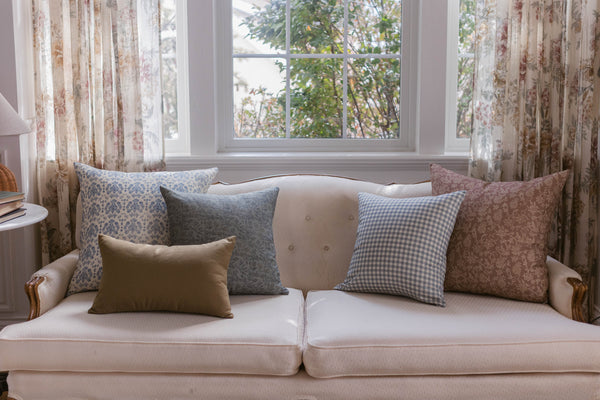 Beige linen pillow with button tufting displayed on a cream sofa with coordinating patterned pillows.