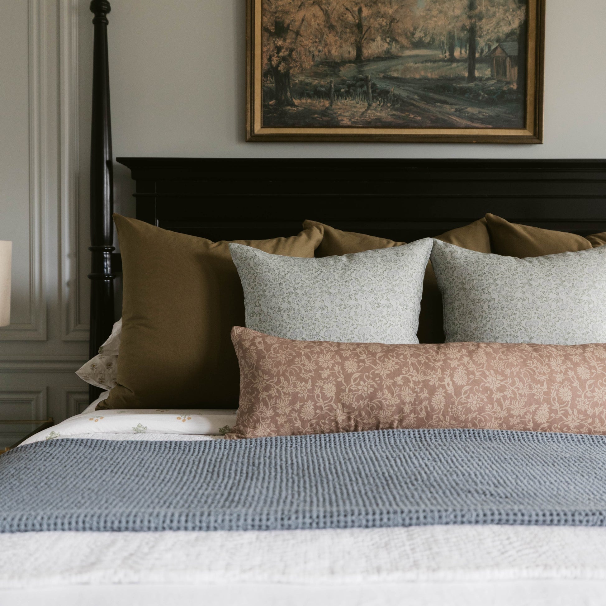 Blue textured bedspread layered with patterned and solid pillows on a black four-poster bed.