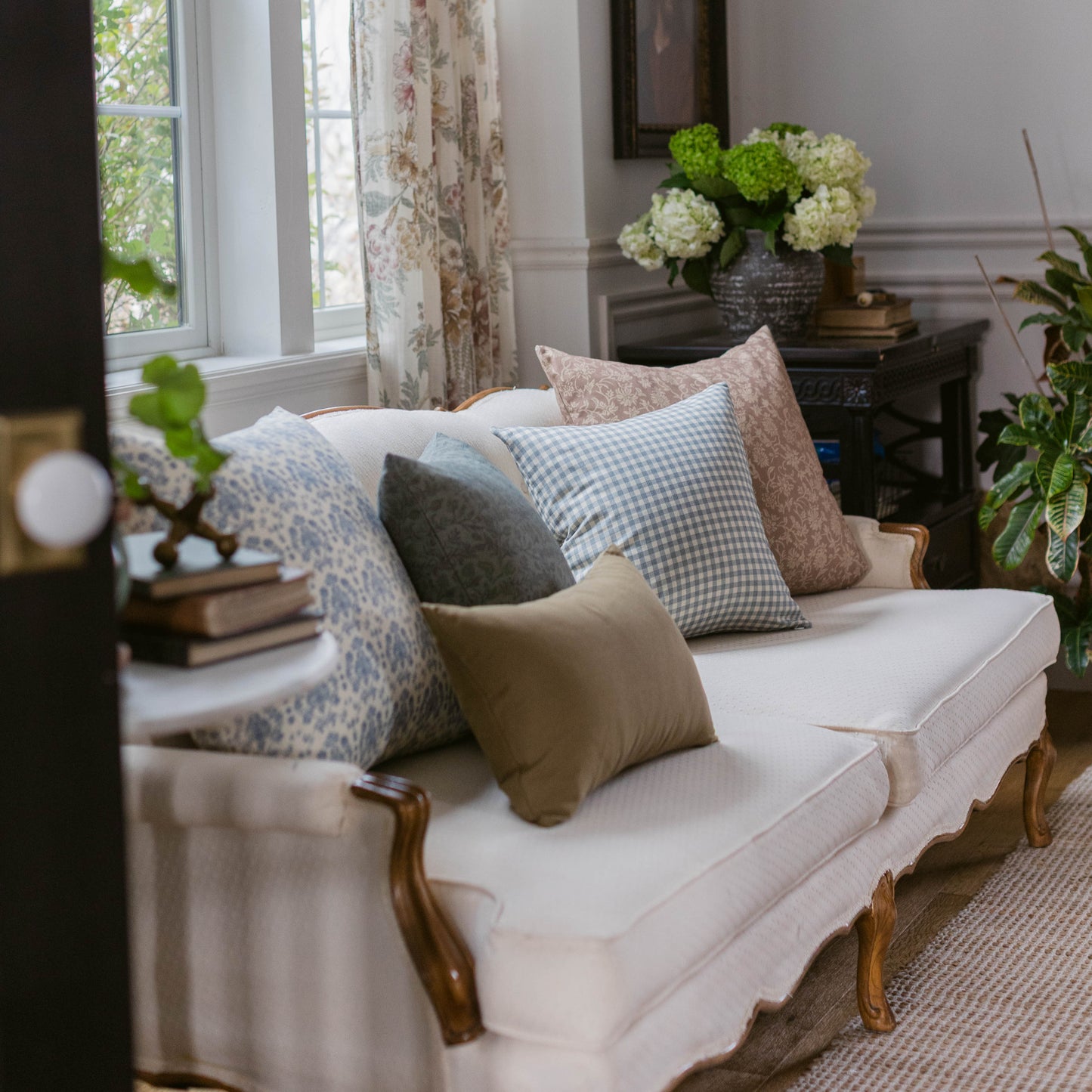 Dusty blue gingham check pillow displayed on cream sofa with coordinating patterned pillows in living room setting.