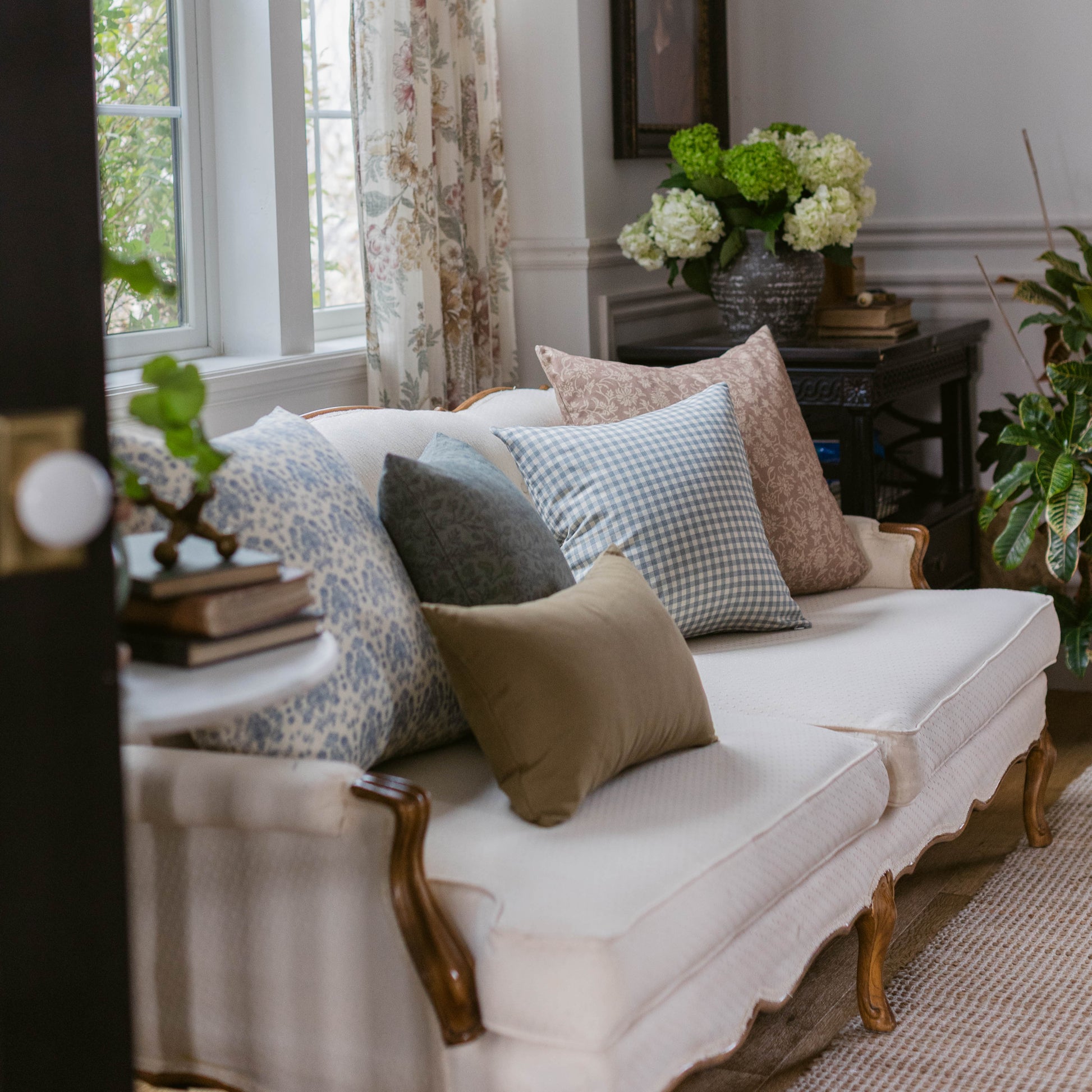 Dusty blue gingham check pillow displayed on cream sofa with coordinating patterned pillows in living room setting.