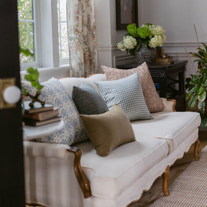 Dusty blue gingham check pillow displayed on cream sofa with coordinating patterned pillows in living room setting.