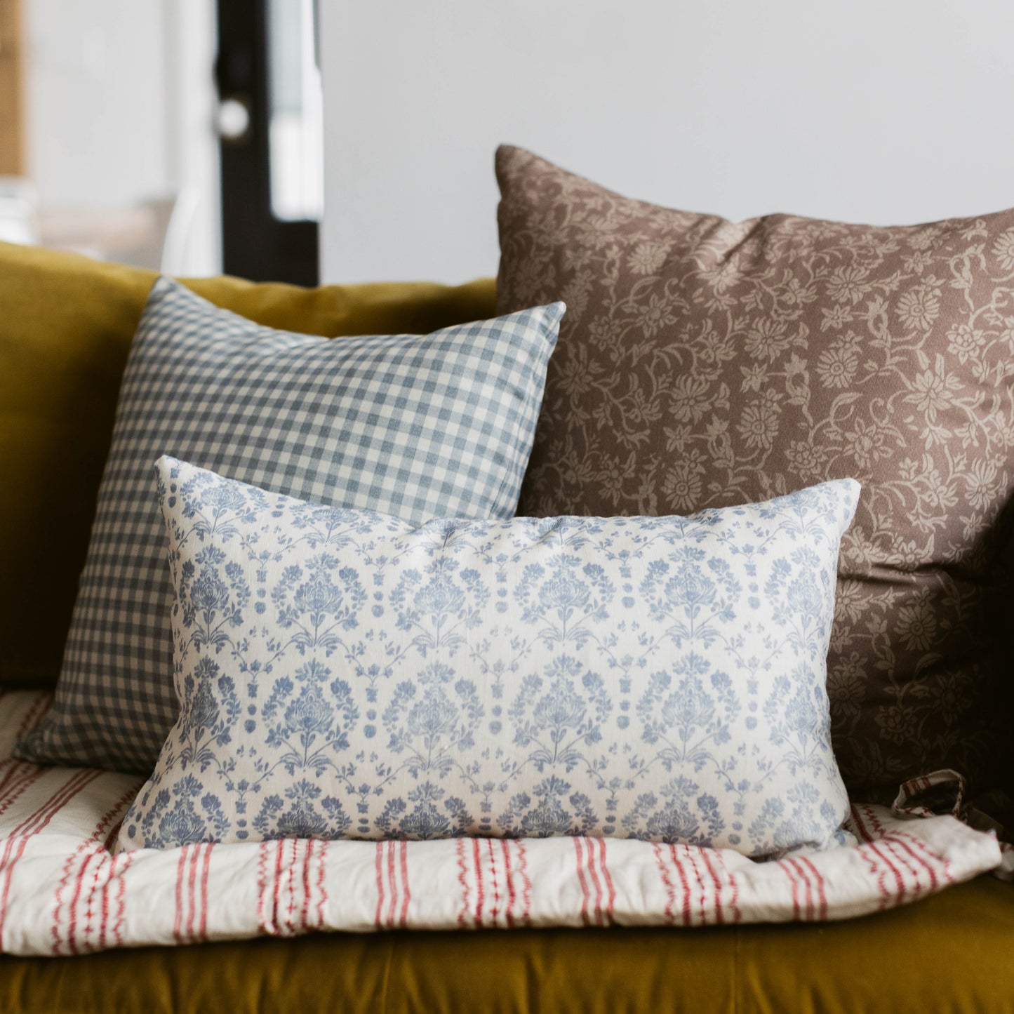 Dusty blue and white gingham pillow cover displayed on a couch with coordinating pillows.
