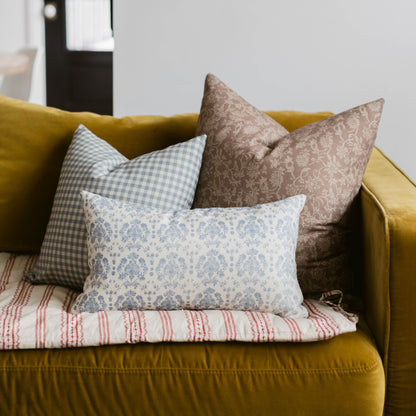 Blue and white damask linen pillow displayed on yellow sofa with coordinating gingham and patterned pillows.