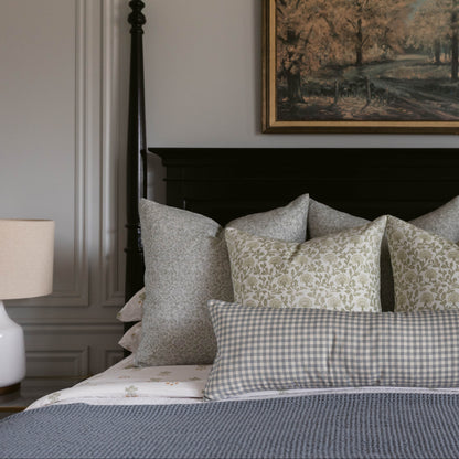 Bed with layered linen pillows in neutral tones featuring solid, plaid, and floral patterns.