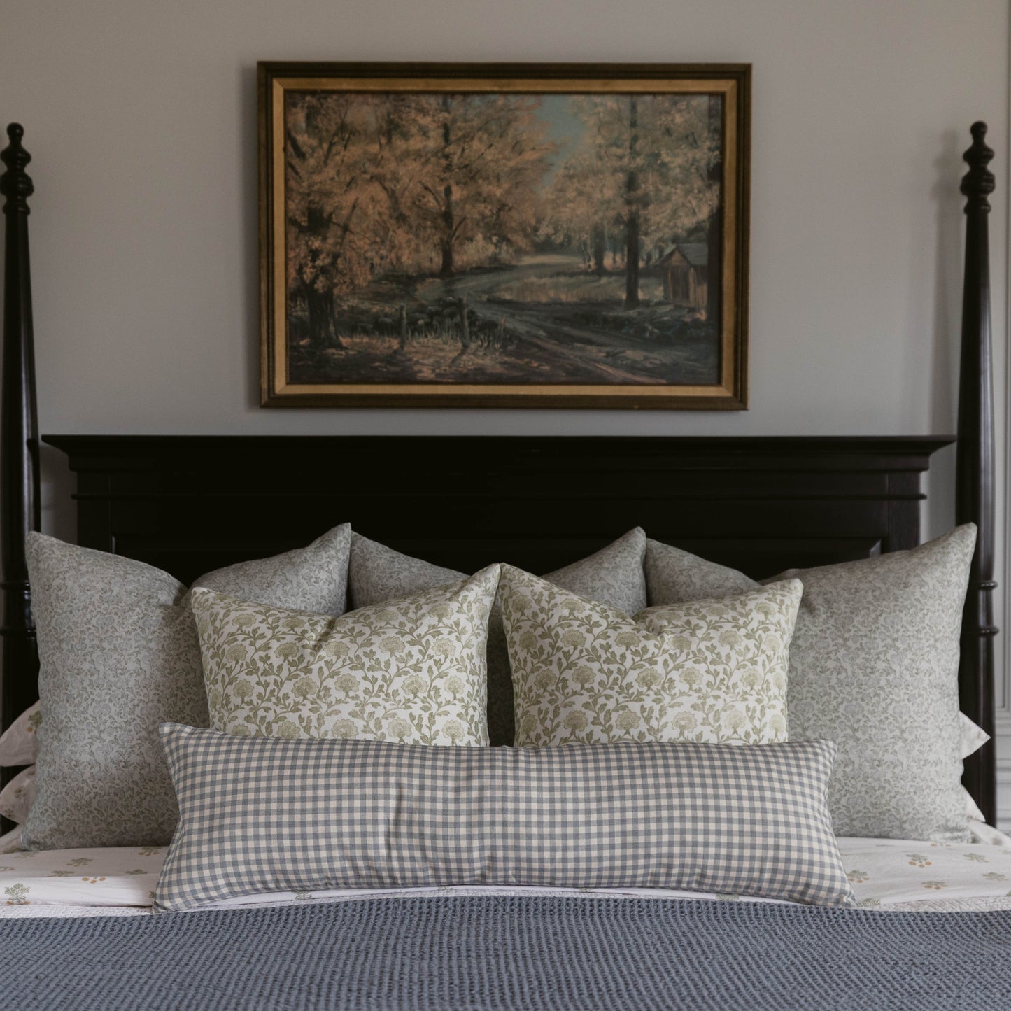 Gray and cream linen pillows with subtle floral and gingham patterns arranged on a bed with black headboard.