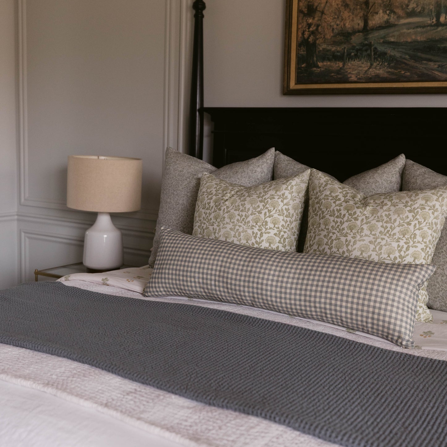 Dusty blue gingham pillow displayed on bed with gray and patterned decorative pillows.