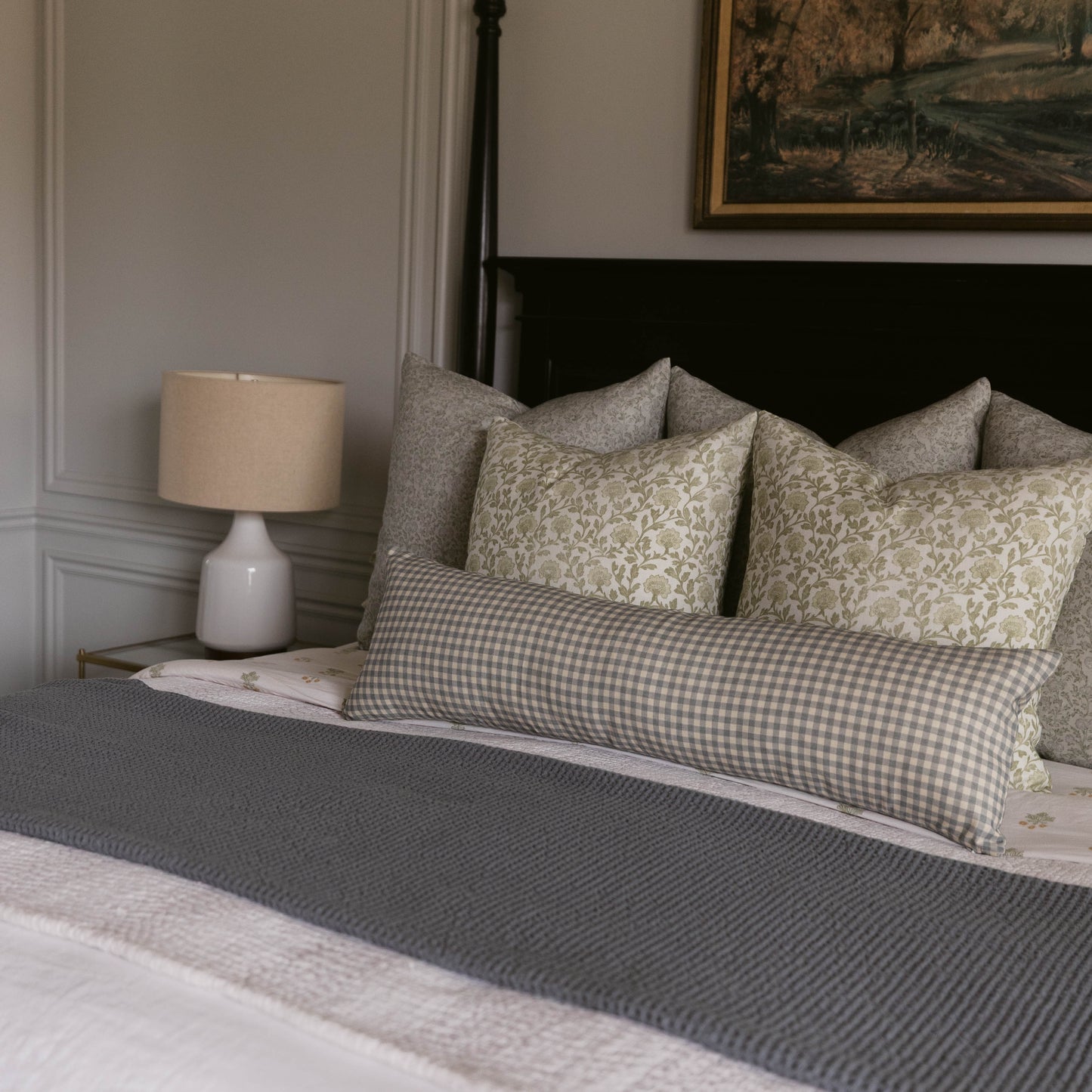 Linen pillow with gingham check pattern in gray and cream, displayed on a bed with matching patterned pillows.