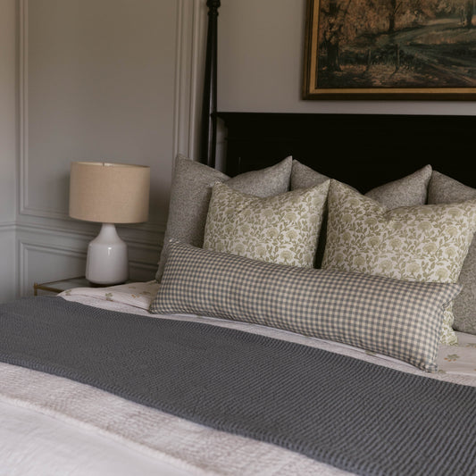 Linen pillow with gingham check pattern in gray and cream, displayed on a bed with matching patterned pillows.