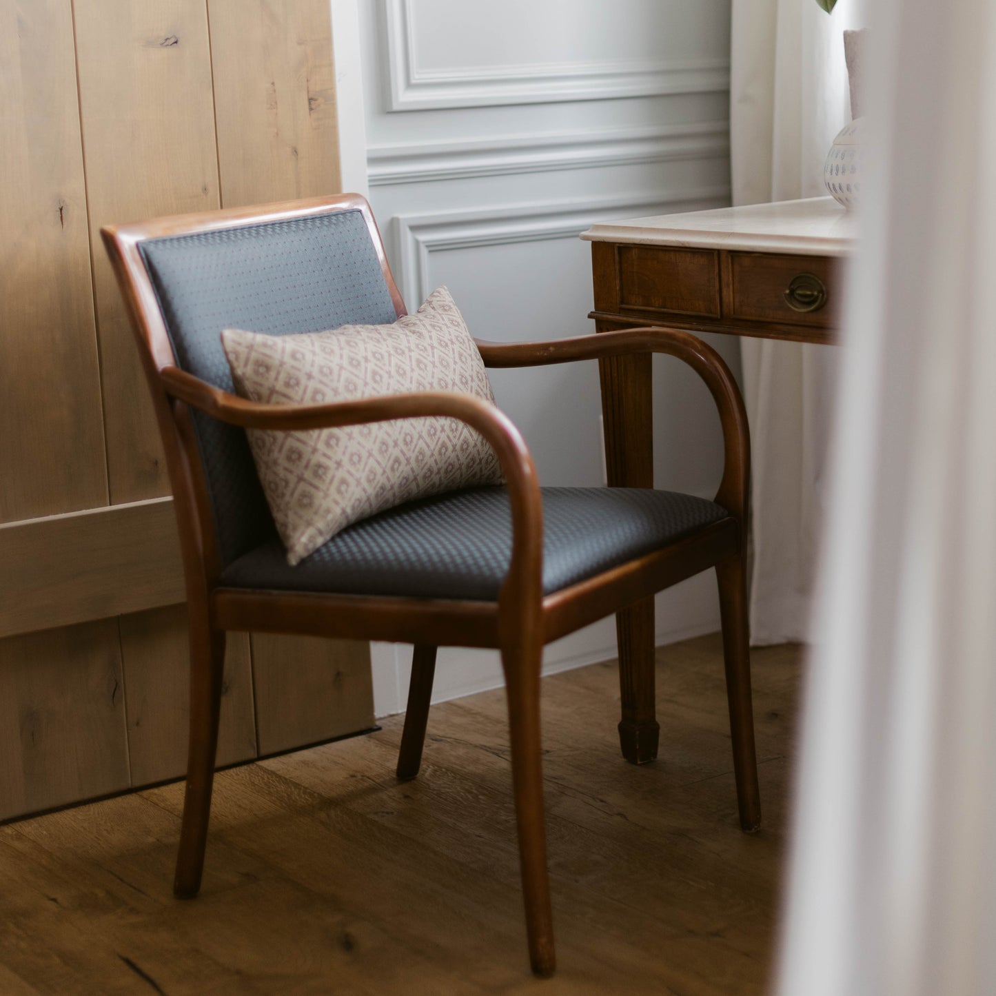 Mid-century modern wooden armchair with blue upholstered seat and back, featuring a cream geometric patterned pillow.