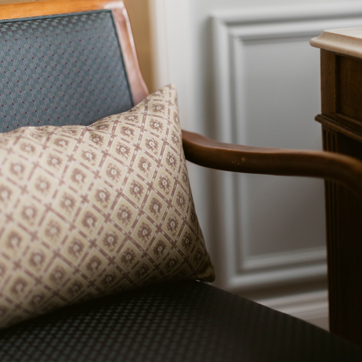 Rectangular pillow with geometric diamond pattern in beige and cream tones on wooden chair with dark seat cushion.