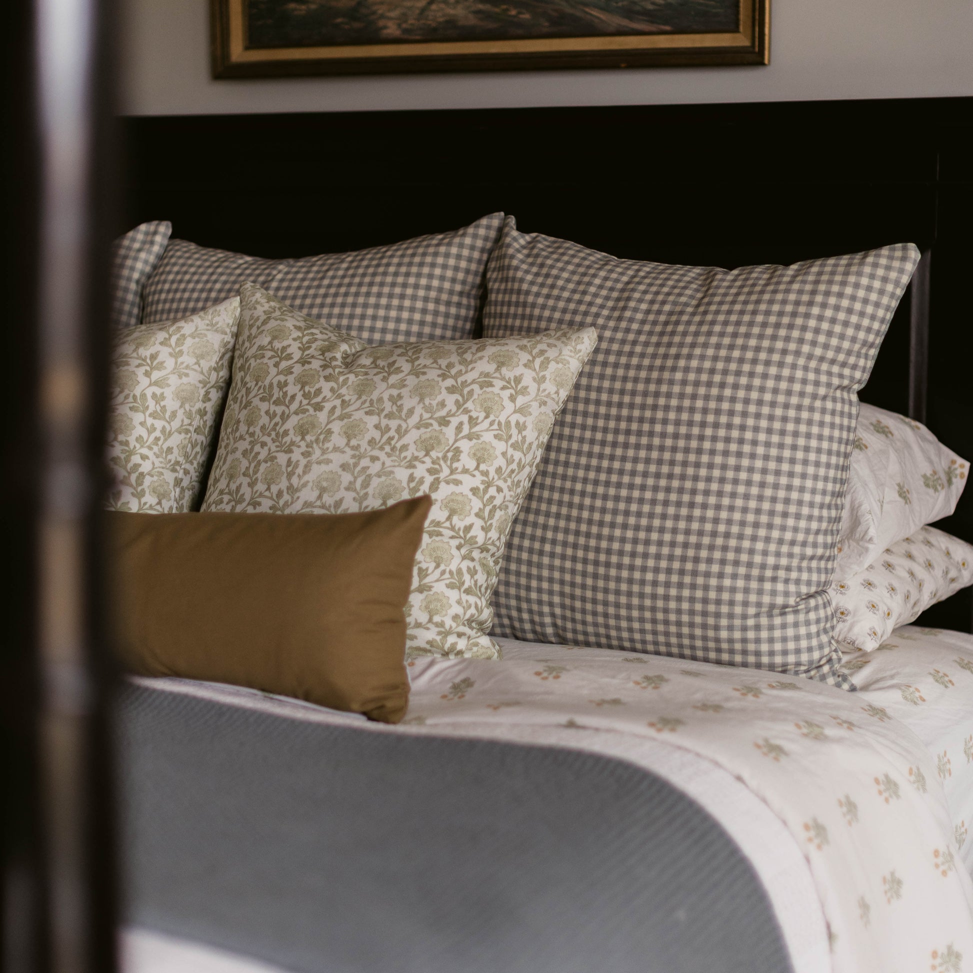 Gray and white gingham linen pillow displayed on a bed with coordinating patterned pillows.